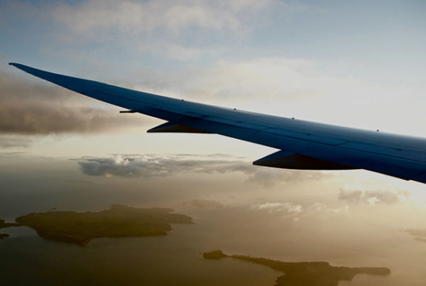 The wing of a plane with clouds in the background.